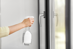 hygiene, health care and safety concept - close up of female hand cleaning window handle surface with detergent spray