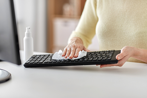 hygiene and disinfection concept - close up of woman cleaning computer keyboard with paper tissue