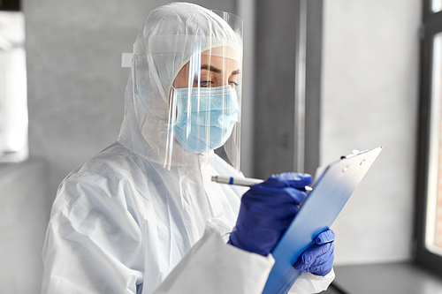health safety, medicine and pandemic concept - close up of female doctor or scientist in protective wear, medical mask, gloves and face shield for protection from virus disease with clipboard