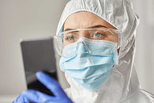 health safety, medicine and pandemic concept - close up of female doctor or scientist in protective wear, medical mask, gloves and goggles for protection from virus disease with smartphone