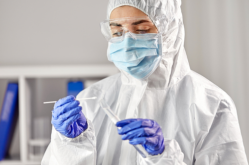 medicine, health and virus concept - close up of young female doctor or scientist in face protective medical mask, goggles and gloves holding beaker with coronavirus test and cotton swab