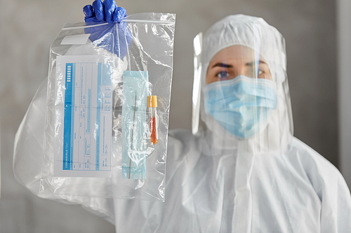 medicine, health and pandemic concept - close up of young female doctor or scientist in protective medical mask, face shield and glove holding zipper bag with test samples and medical report