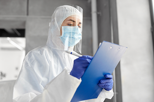 health safety, medicine and pandemic concept - close up of female doctor or scientist in protective wear, medical mask, gloves and face shield for protection from virus disease with clipboard