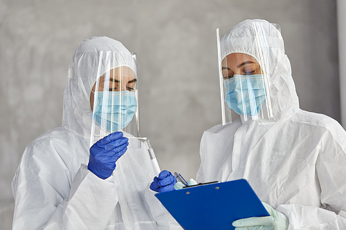 health safety, medicine and pandemic concept - female doctors or scientists in protective wear, medical masks, gloves and face shields with clipboard, test tube and cotton swab