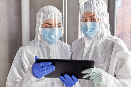 health safety, medicine and pandemic concept - female doctors or scientists in protective wear, medical masks, gloves and face shields for protection from virus disease with tablet computer