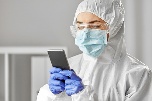 health safety, medicine and pandemic concept - close up of female doctor or scientist in protective wear, medical mask, gloves and goggles for protection from virus disease with smartphone
