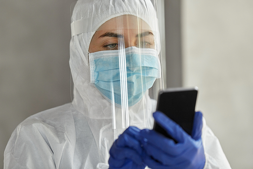 health safety, medicine and pandemic concept - close up of female doctor or scientist in protective wear, medical mask, gloves and face shield for protection from virus disease with smartphone