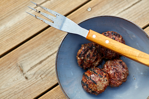 cooking, barbecue and fast food concept - close up of roasted meat cutlets on plate with barbeque fork