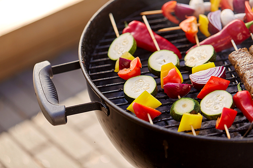 cooking, barbecue and food concept - close up of vegetables on bamboo skewers roasting on brazier grill outdoors
