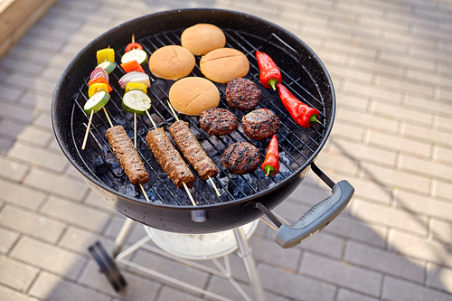 cooking, barbecue and food concept - close up of shish kebab meat, s on bamboo skewers, burger buns and cutlets roasting on brazier grill outdoors