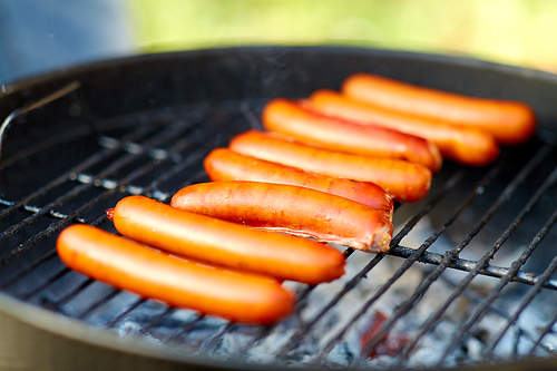 cooking, barbecue and food concept - close up of meat sausages roasting on hot brazier grill