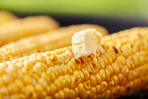 cooking, barbecue and food concept - close up of corn with melting butter roasting on brazier grill outdoors
