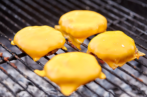 cooking, barbecue and fast food concept - close up of burger meat cutlets with processed cheese roasting on brazier grill outdoors