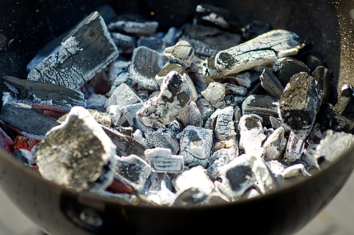 cooking, heat and fire concept - close up of charcoal smoldering in brazier outdoors