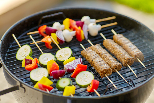 cooking, barbecue and food concept - close up of shish kebab meat and s on bamboo skewers roasting to hot brazier grill outdoors