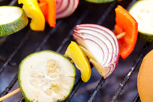 cooking, barbecue and food concept - close up of vegetables on bamboo skewers roasting on brazier grill outdoors