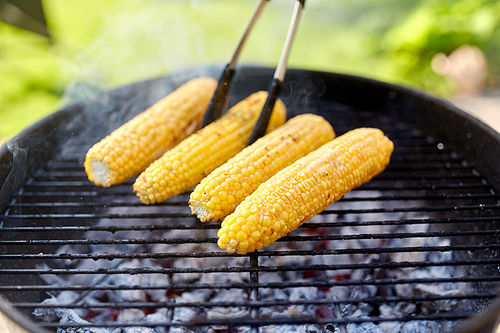 cooking, barbecue and food concept - close up of corn roasting on brazier grill outdoors