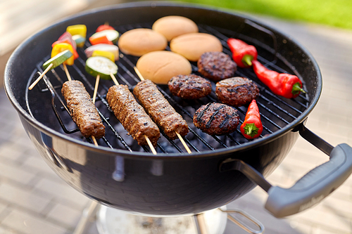 cooking, barbecue and food concept - close up of shish kebab meat, s on bamboo skewers, burger buns and cutlets roasting on brazier grill outdoors