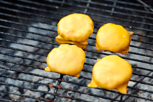 cooking, barbecue and fast food concept - close up of burger meat cutlets with processed cheese roasting on brazier grill outdoors