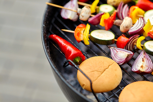 cooking, barbecue and food concept - close up of vegetables on bamboo skewers and burger buns roasting on brazier grill outdoors
