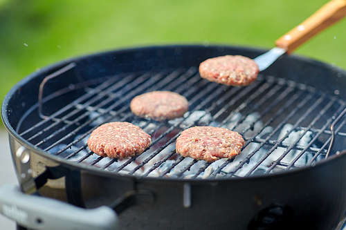 cooking, barbecue and fast food concept - close up of burger meat cutlets roasting on brazier grill outdoors
