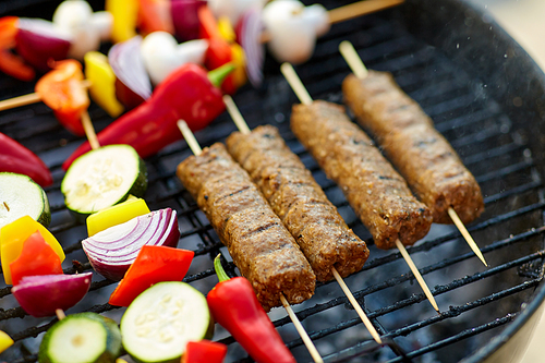 cooking, barbecue and food concept - close up of shish kebab meat and s on bamboo skewers roasting to hot brazier grill outdoors