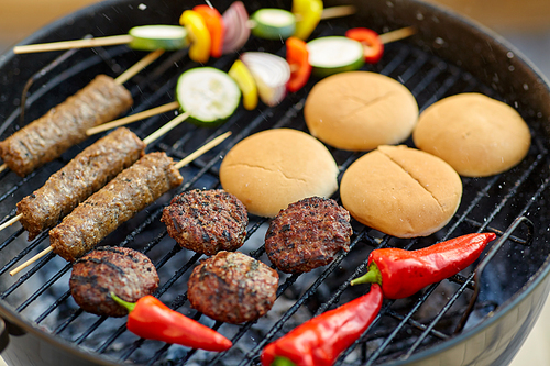 cooking, barbecue and food concept - close up of shish kebab meat, s on bamboo skewers, burger buns and cutlets roasting on brazier grill