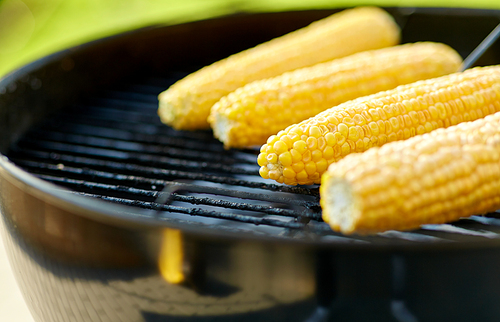 cooking, barbecue and food concept - close up of corn roasting on brazier grill outdoors