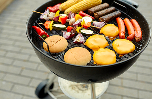 cooking, barbecue and food concept - close up of shish kebab meat, s on bamboo skewers, burger buns with corn and sausages roasting on brazier grill outdoors