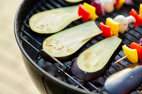 cooking, barbecue and food concept - close up of eggplant slices and vegetables with champignon mushrooms on bamboo skewers roasting on hot brazier grill outdoors