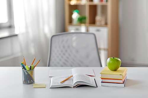 education and learning concept - books, apple and school supplies on table at home