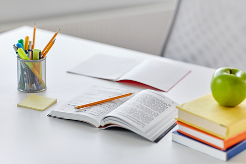 education and learning concept - books, apple and school supplies on table at home