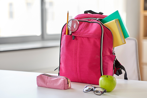 education and learning concept - pink backpack with books and school supplies, green apple on table at home