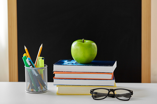 education and learning concept - books, apple, chalkboard and school supplies on table at home