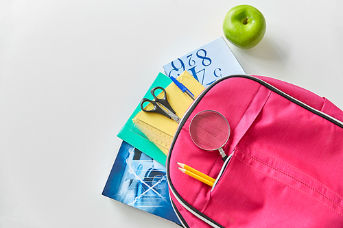 education and learning concept - pink backpack with books and school supplies, green apple on table