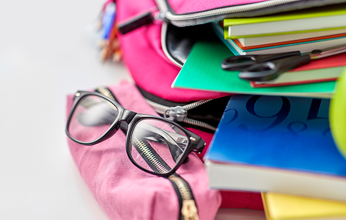 education and learning concept - close up of pink backpack with books and school supplies, green apple on table at home