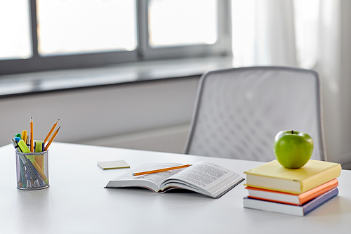 education and learning concept - books, apple and school supplies on table at home