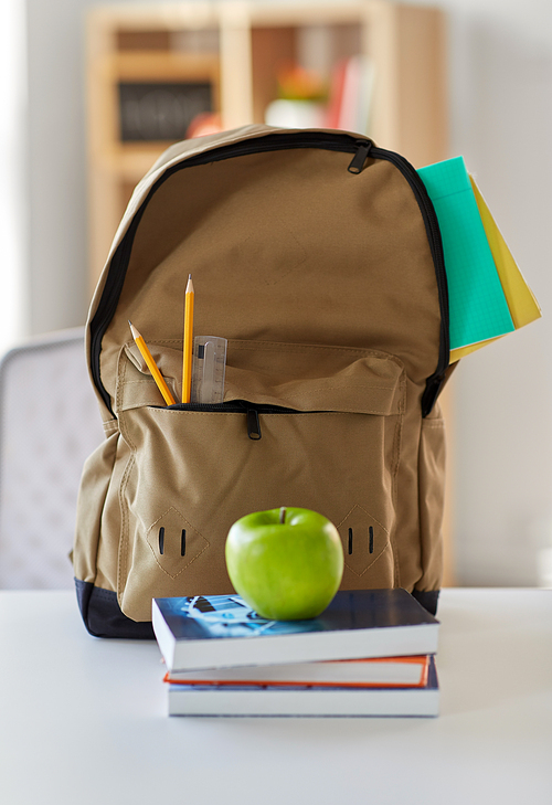 education and learning concept - backpack with books, school supplies and green apple on table at home