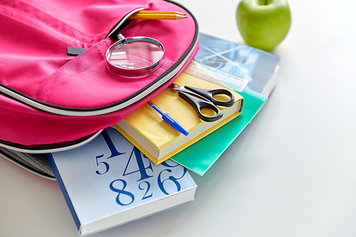 education and learning concept - pink backpack with books and school supplies, green apple on table