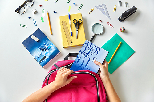 education and learning concept - hands packing pink backpack with books and school supplies on table