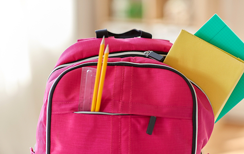 education and learning concept - close up of pink backpack with books and school supplies