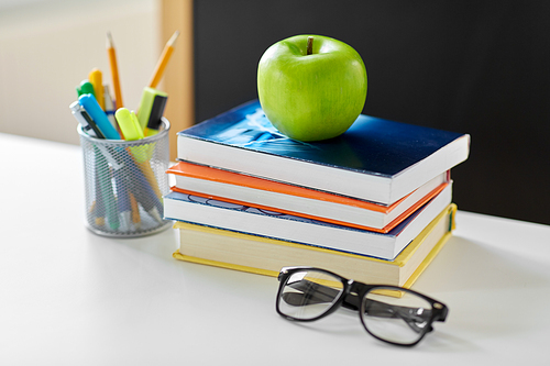 education and learning concept - books, apple, chalkboard and school supplies on table at home