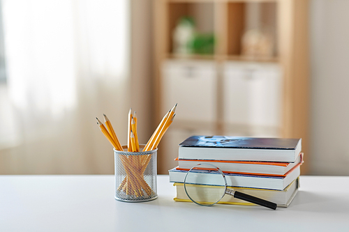 education, school and learning concept - book with magnifier and pencil on table at home