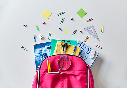 education and learning concept - pink backpack with books and school supplies on table