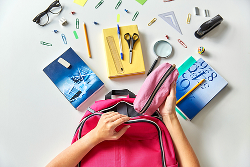 education and learning concept - hands packing pink backpack with pencil-case, books and school supplies on table