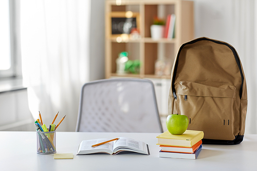 education and learning concept - books, apple and school supplies on table at home