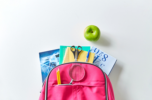 education and learning concept - pink backpack with books and school supplies, green apple on table