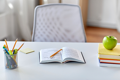 education and learning concept - books, apple and school supplies on table at home