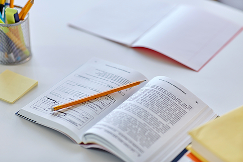 education and learning concept - close up of book, pencil, notebook and school supplies on table