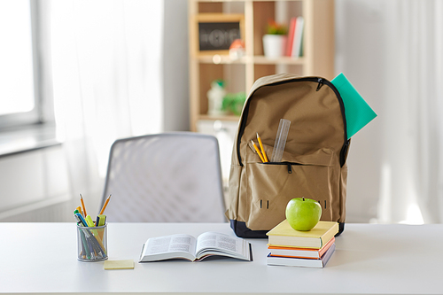 education and learning concept - books, apple and school supplies on table at home